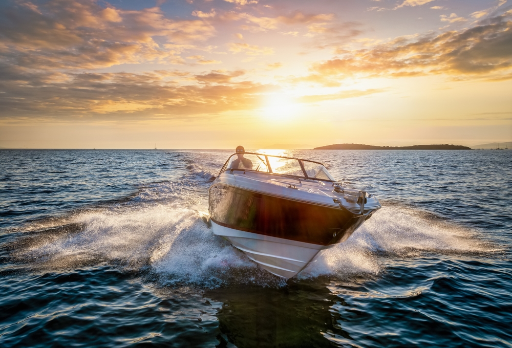 Aerial front view of a sports motor boat cruising with high speed over the blue sea during summer sunset time.