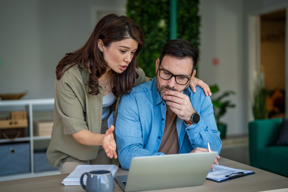 Worried middle-aged couple sitting at a desk reviewing finances on a laptop, representing homeowners assessing insurance risks and expenses.