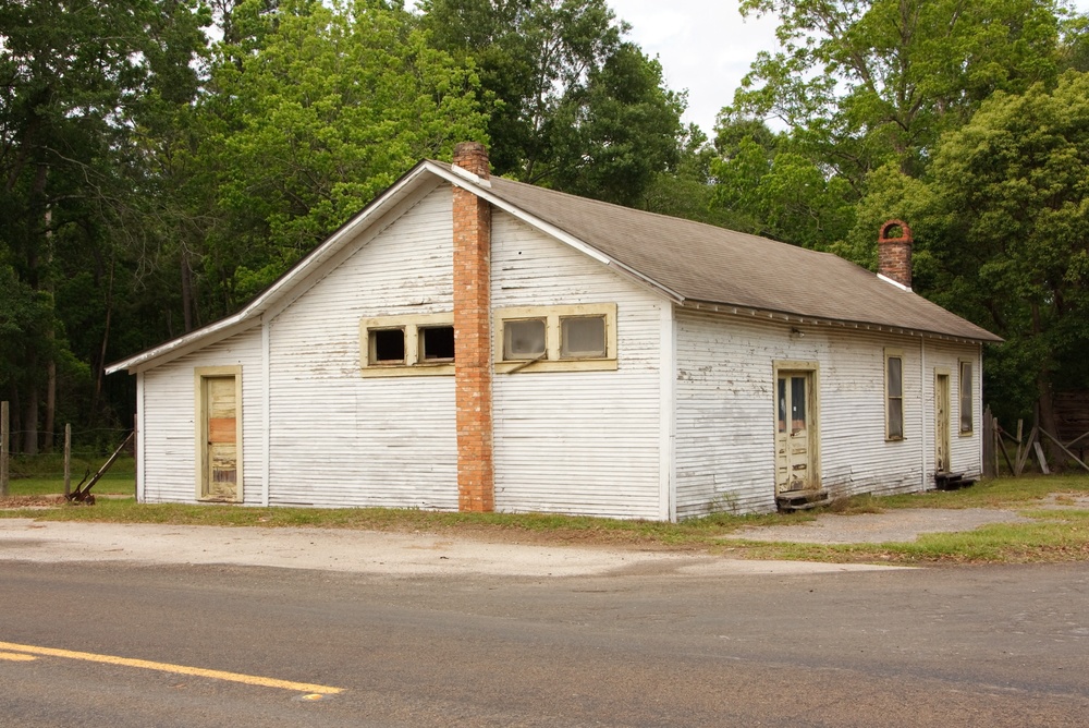 AnAbandonedHouseInTheAfternoonInBunaTexas Vacant single-family house with an overgrown yard and weathered exterior, illustrating the risks associated with an unoccupied property.